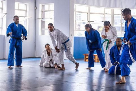 Diverse martial arts class practicing grappling drills in dojo