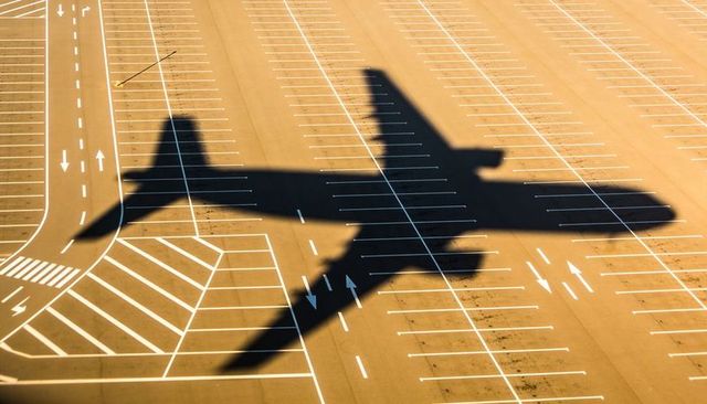 Giant jet shadow casting across empty airport apron with parking lines and runway markings