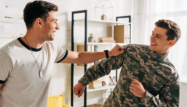 Playful mock-punch between civilian friend and soldier in camo in bright living room