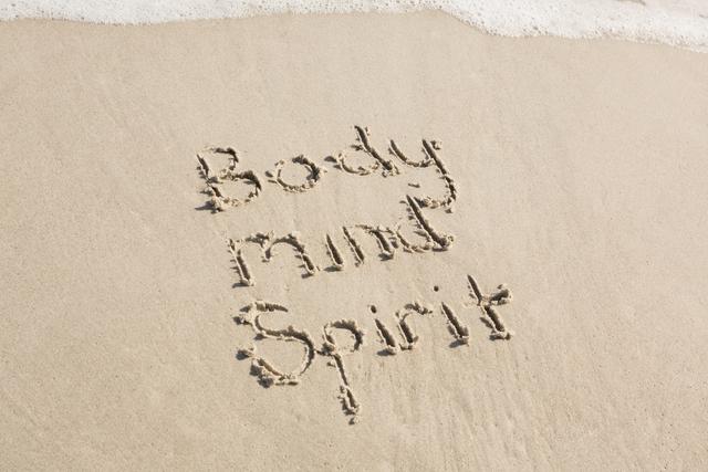 Body mind spirit written on sand at beach
