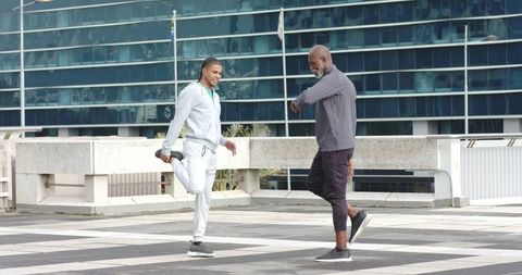 Diverse men stretching and balancing on urban rooftop in tracksuits for fitness