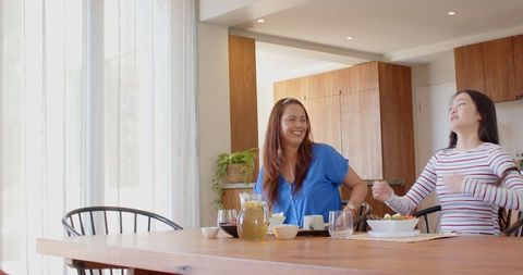 Mother and Daughter Relaxing at Home Dining Table with Salad and Juice