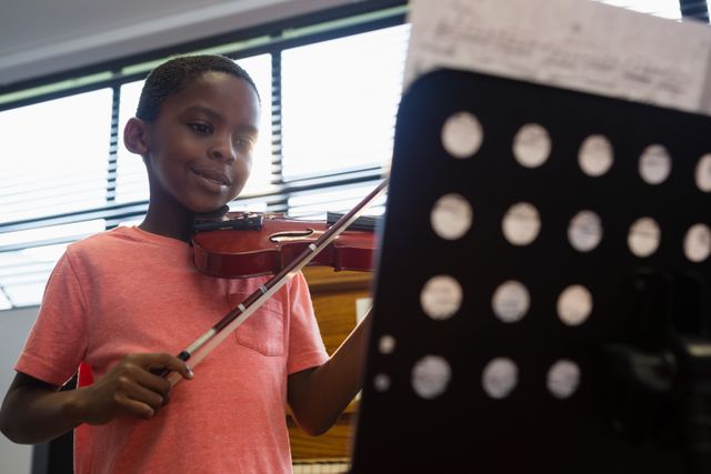 Young boy enthusiastically playing violin in a classroom setting, showcasing his musical talent and dedication. Ideal for educational content, music school promotions, and articles on child development and arts education.