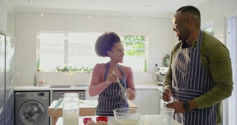 Couple baking together in bright modern kitchen, whisking batter at island and smiling