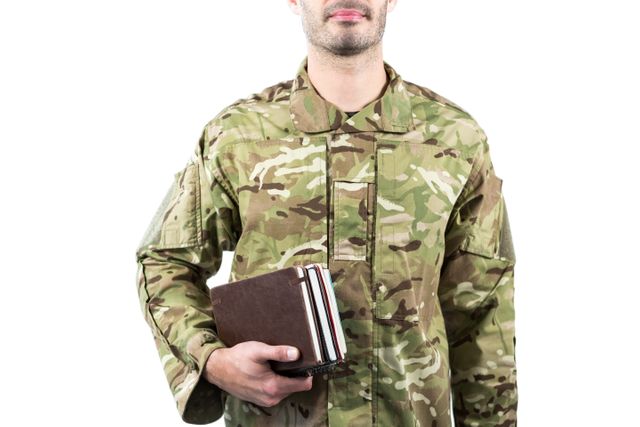 Soldier in camouflage uniform holding books, symbolizing the combination of military service and education. Ideal for use in articles about military education programs, veterans pursuing higher education, or the importance of knowledge in the armed forces.