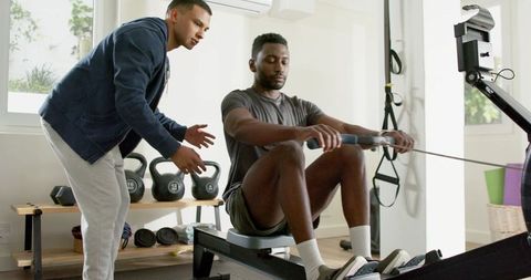 Personal trainer coaching african american man rowing on machine in modern home gym