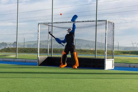 Field hockey goalkeeper blocking shot in energetic defense move