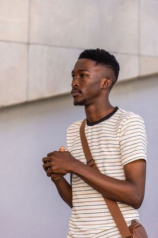Young man standing holding phone brown crossbody bag looking left urban portrait