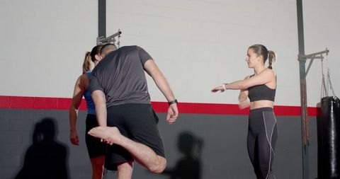 Instructor leading diverse fitness group stretching by red stripe wall with punching bag