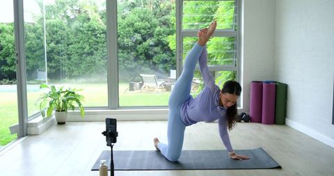 African American woman practicing yoga pose in bright home studio while recording workout