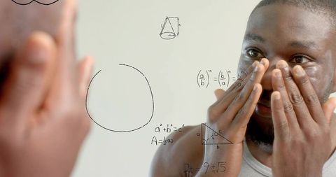 Black man checking eyes in mirror with math equations on glass, reflecting study focus