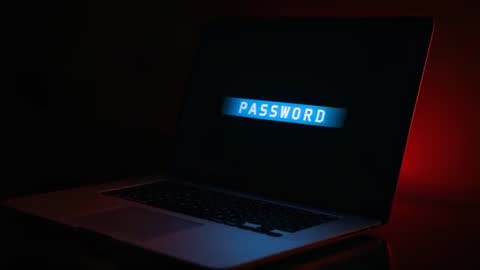 Laptop screen showing PASSWORD prompt pulsing in blue-red rim glow on reflective desk