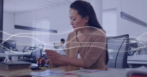 Korean designer using stylus and holding color swatches at modern open office workspace