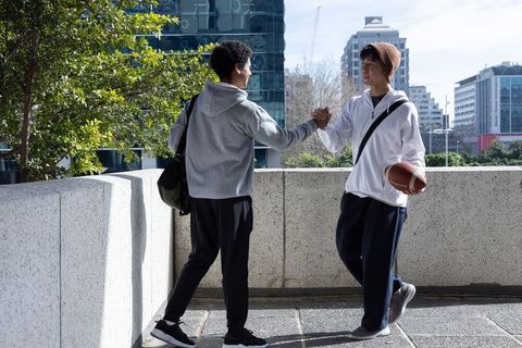 Diverse teen friends greeting on urban terrace holding football in casual sportswear