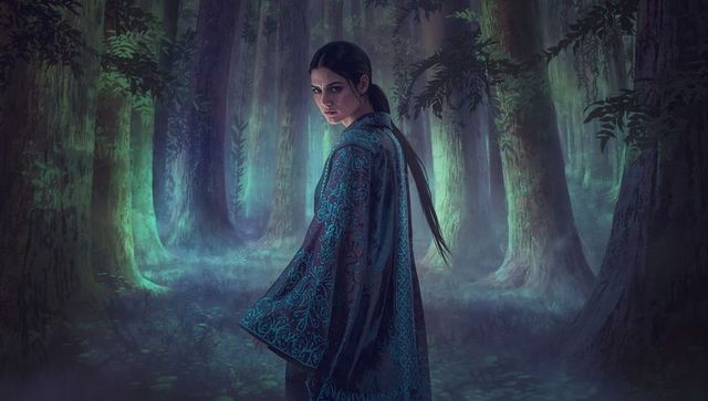 Mystic woman turning in foggy ancient forest wearing ornate teal embroidered robe, twilight