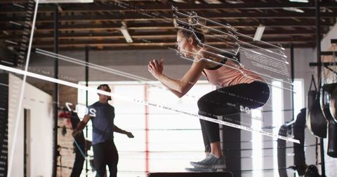 Female athlete performing explosive box jump in industrial gym with trainer