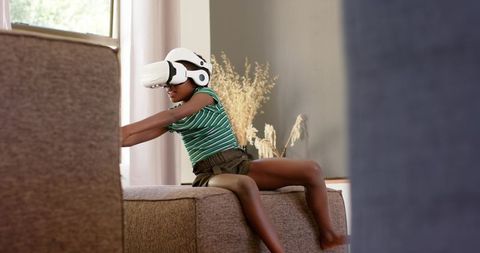African teenage girl experiencing immersive virtual reality adventure on ottoman at home