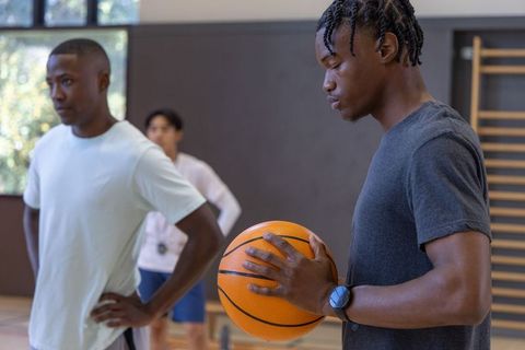 Young black athlete holding basketball, teammates preparing for training in gym