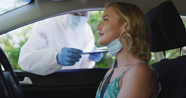 Caucasian woman sitting in car, wearing face mask, having covid test done by medical worker outdoors. health checks and precautions during coronavirus covid 19 pandemic.
