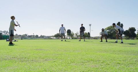 Young men playing casual cricket match on sunny park field practicing batting and fielding