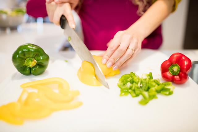 This image shows a mother and daughter cutting bell peppers together in a kitchen. It is ideal for use in articles or advertisements related to family bonding, cooking at home, healthy eating, and food preparation. The vibrant colors of the vegetables and the focus on hands make it visually appealing for culinary blogs, recipe websites, and kitchen appliance promotions.