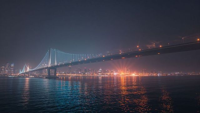 Illuminated Suspension Bridge Over City Skyline After Dusk