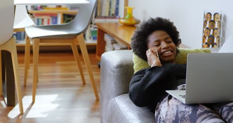 Relaxed Woman on Sofa Using Laptop and Phone at Home