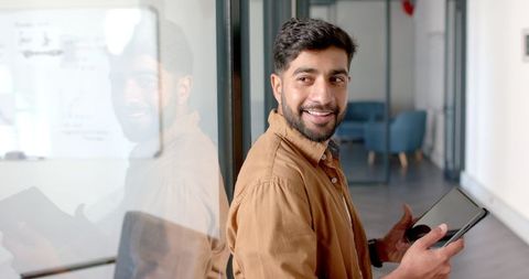 Smiling professional holding tablet in modern office with reflective glass wall