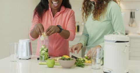 Cheerful friends preparing healthy smoothie together in kitchen
