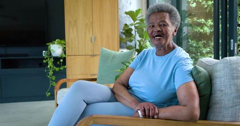 Senior african woman relaxing on wooden sofa in bright living room showing ring