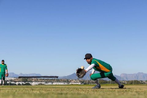 Low-angle outfielder diving to catch baseball with glove on sunny grass field