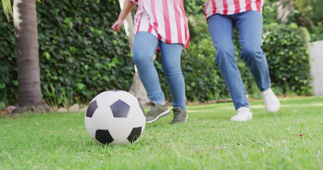 Image of low section of biracial mother and daughter playing soccer in garden. Family, motherhood, relations and spending quality time together concept digitally generated image.