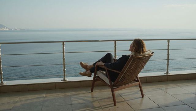 Woman relaxing on balcony chair overlooking calm sea horizon on spacious tiled terrace