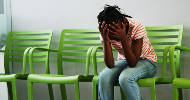 An African American woman appears distressed as she sits alone on a chair, with copy space. Her body language suggests she may be experiencing sadness or anxiety in a waiting area.