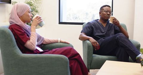 African american nurse and muslim colleague relaxing in staff lounge drinking coffee