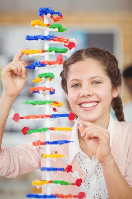 Young girl in a school laboratory smiling while working on a colorful molecule model. Ideal for educational content, science class promotions, STEM programs, and materials highlighting hands-on learning and student engagement in scientific experiments.