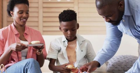African american family sharing snack time on sofa, parents and son enjoying pastries