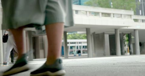 Urban pedestrian walking across concrete plaza in gray skirt and sneakers with motion blur