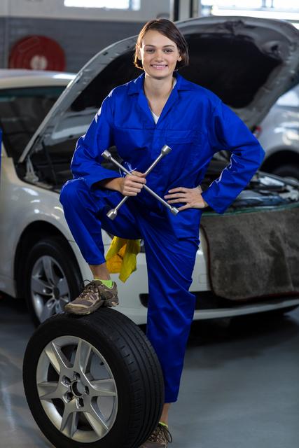 Portrait of female mechanic standing with a tyre in repair garage