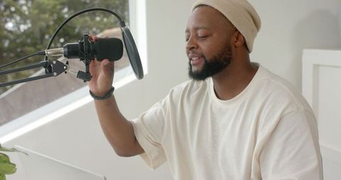 Podcaster recording in bright home studio reaching for microphone with pop filter