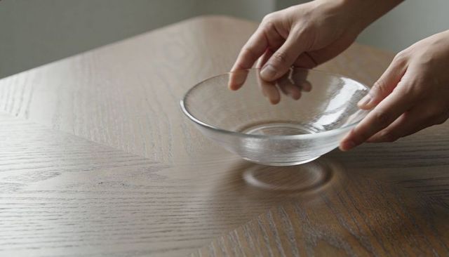 Hands placing clear glass bowl on wooden dining table minimalist calm translucent dish