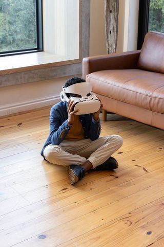 Preteen boy adjusting white vr headset while sitting on wood floor in modern living room