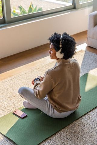 Black woman meditating on home yoga mat wearing headphones and smartwatch