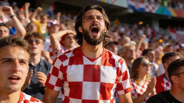 Passionate football fan cheering in red white checkered jersey among stadium crowd