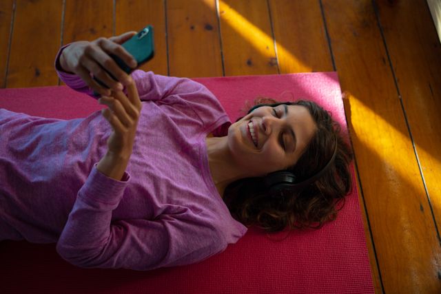 Smiling biracial woman lying on floor, using smartphone in sunny cottage living room. healthy living, close to nature in rural home.