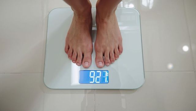Standing barefoot weighing on glass digital bathroom scale with backlit blue lcd 92.7
