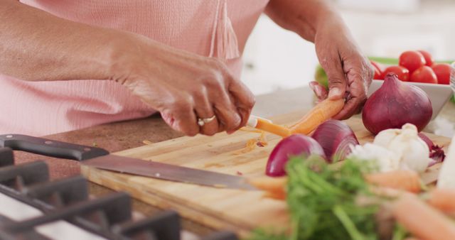 This image depicts hands of a woman slicing fresh carrots and other vegetables on a wooden cutting board in a kitchen. Useful for content related to cooking, healthy eating, food preparation, and lifestyle. Suitable for use on culinary blogs, recipes, and nutrition websites.