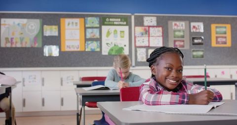 Smiling girl writing in classroom with distant classmate