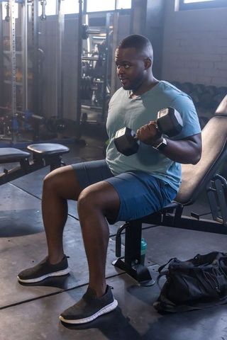 African-american man performing seated dumbbell curl on adjustable bench in gym