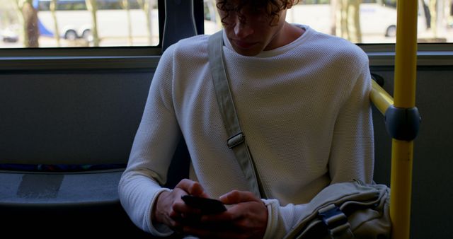 Biracial man sitting in city bus using smartphone. Communication, transport, city living and lifestyle, unaltered.